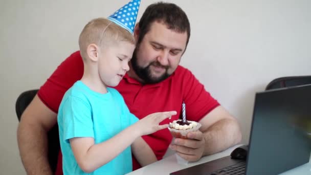 Niño con su padre celebrar cumpleaños en línea, hablando por cuaderno con familiares y amigos. Apaga la vela. — Vídeos de Stock
