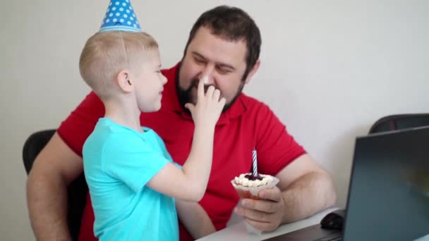 Mały chłopiec z ojcem świętują urodziny online, rozmawiając przez notatnik z krewnymi i przyjaciółmi. Zdmuchnij świeczkę. — Wideo stockowe