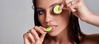 Evde konsept yüz bakımı. Yüzünde salatalık olan güzel bir kadının portresi.