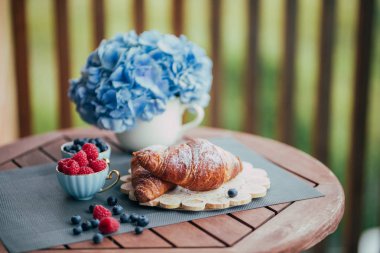 Balkonda sabah kahvaltısı, kruvasan, kahve ve böğürtlen.