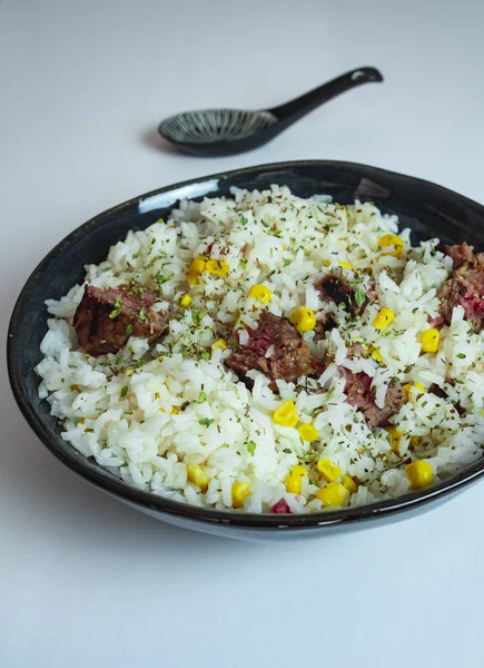 Tigela de porcelana escura de arroz branco com milho, hambúrguer e orégano. E uma colher preta. Placa mediterrânica . — Fotografia de Stock