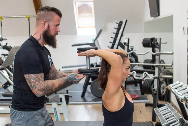 Bearded coach helps a woman in a gym.