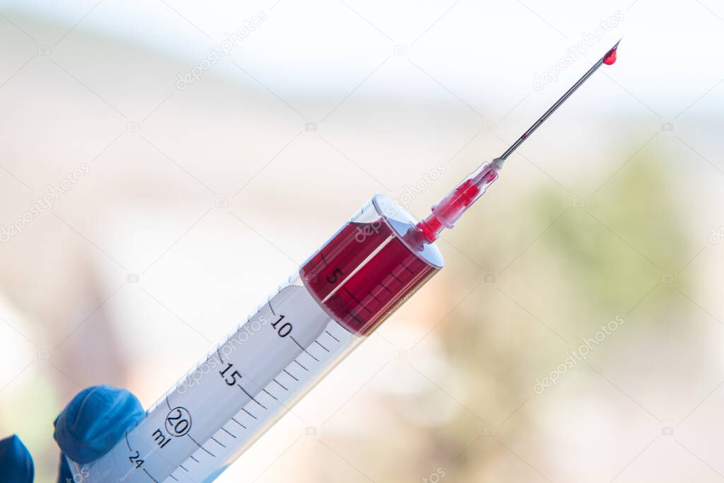 Injection syringe with blood with gloved hand.
