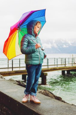 İsviçre Cenevre Gölü yanında duran büyük renkli şemsiye tutan üzerinde sıcak yeşil ceket, sevimli küçük bir kız, açık portresi