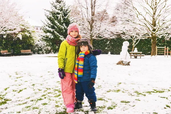 Two adorable kids playing together in snow park, wearing warm winter clothes — Stock Photo, Image