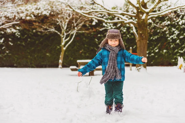 Χαριτωμένο μικρό αγόρι που παίζει στο χειμερινό πάρκο. Το παιδί έχοντας διασκέδαση σε εξωτερικούς χώρους, τρέχει στο χιόνι, φορώντας ζεστό μπλε μπουφάν, καπέλο και κασκόλ — Φωτογραφία Αρχείου