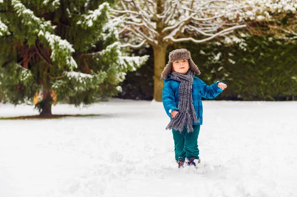 Söpö poika leikkimässä talvipuistossa. Lapsi pitää hauskaa ulkona, juoksee lumella, yllään lämmin sininen takki, hattu ja huivi — kuvapankkivalokuva