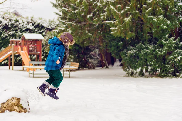 Söt liten pojke spelar i Vinterparken. Kid har roligt utomhus, kör på snö, bär varma blå jacka, mössa och halsduk — Stockfoto