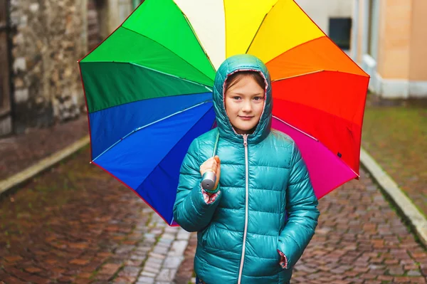 Outdoor portrait of a cute little girl, wearing warm green jacket, holding big colorful umbrella — Stock Photo, Image