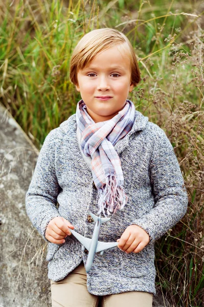 Портрет очаровательного мальчика в трикотажной куртке и стильном шарфе, с маленьким игрушечным самолетом — стоковое фото