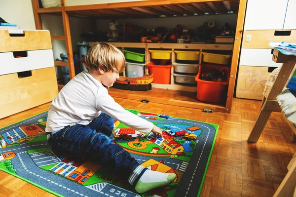 Bonito menino brincando sozinho no tapete de brinquedo em seu quarto em casa — Fotografia de Stock