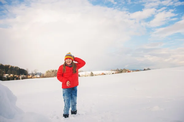 Lilla flickan bär röd jacka och färgglada hatt, leker med snö på vintern — Stockfoto