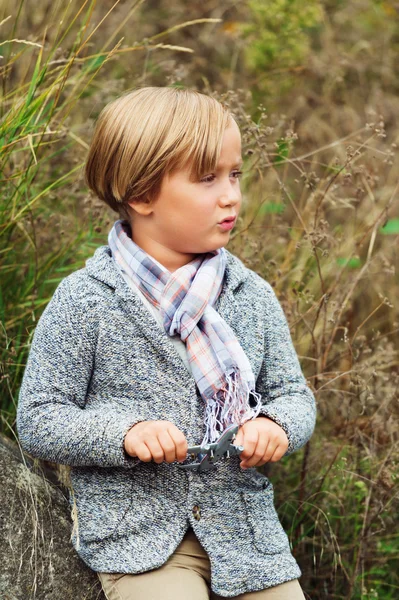 Outdoor fashion portrait of adorable little boy wearing  knitted jacket and stylish scarf, holding small toy airplane — Stock Photo, Image