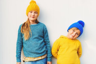 Çok güzel moda çocuklar, sıcak pullovers ve şapkalar, karşı Beyaz ahşap arka plan ayakta açık portresi