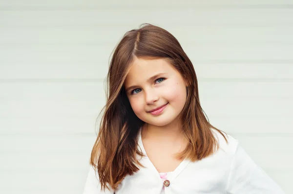 Outdoor portrait of cute little 8-9 year old girl with brown hair, wearing white jacket, standing against white background — Stock Photo, Image