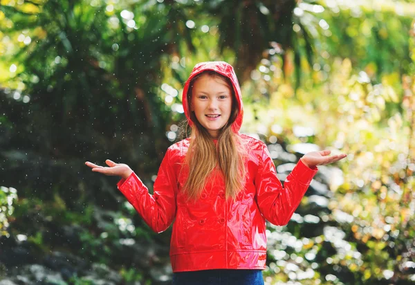 Entzückendes kleines 9-jähriges Mädchen spielt im Regen im Park in roter Vinyljacke — Stockfoto