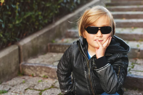 Ritratto all'aperto di adorabile bambino biondo che indossa giacca di pelle nera e occhiali da sole — Foto Stock