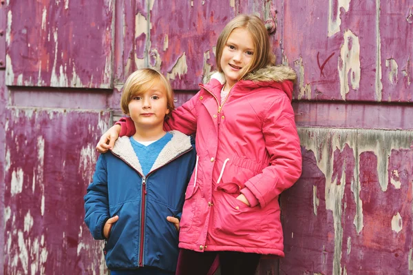 Portret van twee schattige kinderen buitenshuis, het dragen van warme jassen permanent naast oude paarse achtergrond — Stockfoto