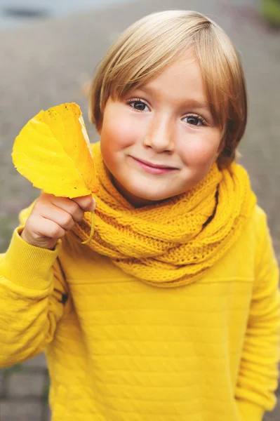 Autumn close up portrait of adorable little boy with leaf, wearing yellow warm sweatshirt and knitted scarf — Stock Photo, Image