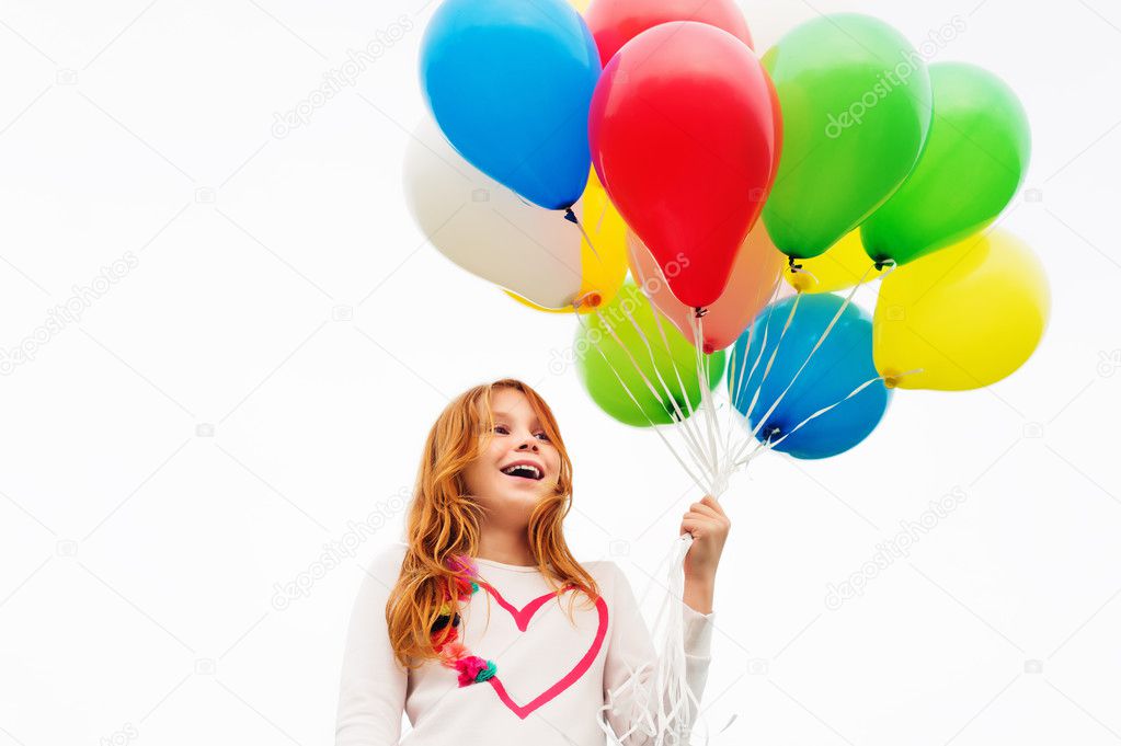 Happy little 8-9 year old girl with red hair holding colorful helium balloons