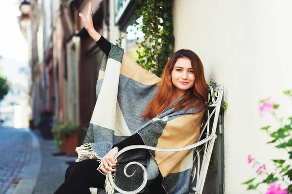 Moda młody 20-letnia dziewczyna siedzi na ławce, na sobie ciepłą kurtkę plaid — Zdjęcie stockowe