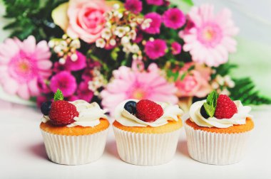tereyağı krema ve taze çilek, arka plan üzerinde Pembe buket ile 3 cupcake