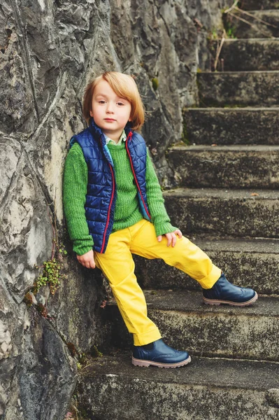 Utomhus mode porträtt av bedårande lilla 4-åriga pojke, klädd i blå väst och stövlar, gula byxor och grön tröja — Stockfoto