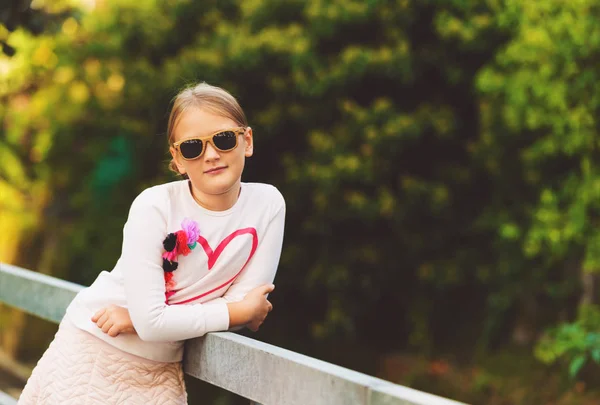 Mode Porträtt av en söt liten flicka utomhus, klädd i vit tröja med hjärta och solglasögon — Stockfoto