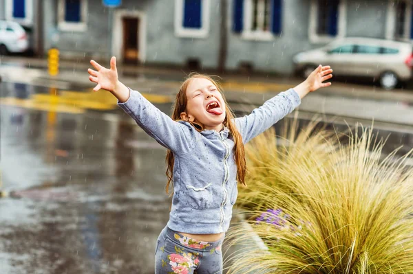 可爱的小女孩抓雨滴与她的舌头，张开双臂 — 图库照片