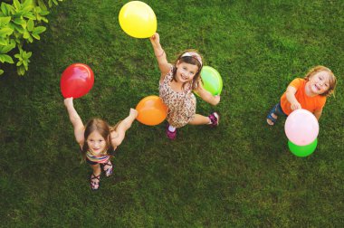 Mutlu üç küçük renkli balonlar ile açık havada, üstten görünüm oynayan çocuklar