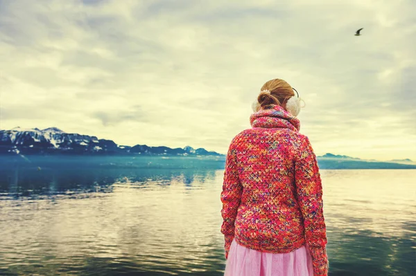 Adorable little girl admiring lake Geneva on a cold winter day, wearing warm pink pullover and earmuffs, back view — Stock Photo, Image