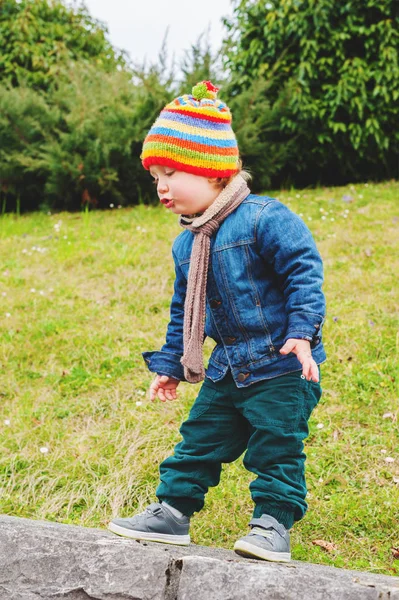 Menino adorável brincando no parque, vestindo chapéu colorido, jaqueta de ganga e calças verdes — Fotografia de Stock