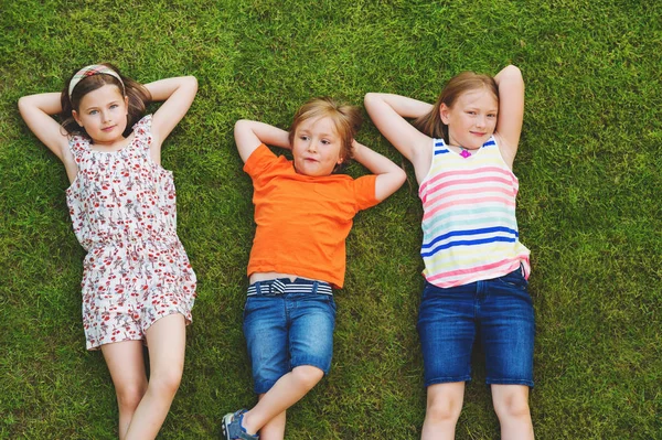 屋外楽しい幸せな様子。夏の公園で遊ぶ子供たち。小さな男の子と新鮮な緑の草を置く 2 つの女の子 — ストック写真