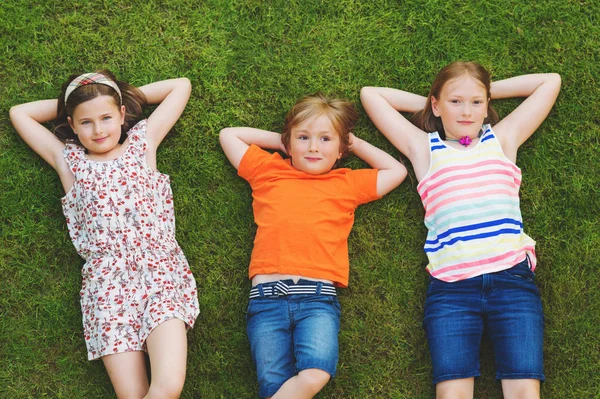 Crianças felizes se divertindo ao ar livre. Crianças brincando no parque de verão. Menino e duas meninas deitado na grama fresca verde — Fotografia de Stock