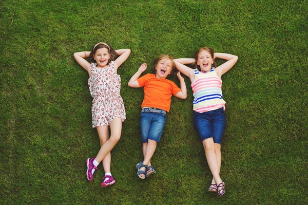 Crianças felizes se divertindo ao ar livre. Crianças brincando no parque de verão. Menino e duas meninas deitado na grama fresca verde — Fotografia de Stock