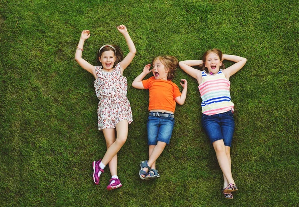 Crianças felizes se divertindo ao ar livre. Crianças brincando no parque de verão. Menino e duas meninas deitado na grama fresca verde — Fotografia de Stock