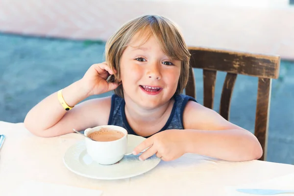 Retrato ao ar livre de um menino bonito bebendo chocolate quente no café — Fotografia de Stock