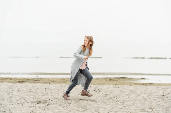 Gri pantolon ve uzun hırka giymiş 8-9 yaşında göl kenarında oynayan sevimli küçük kız — Stok fotoğraf