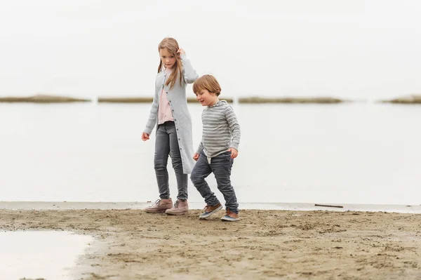 Two little kids playing outdoors by the lake, wearing grey clothes — Stock Photo, Image