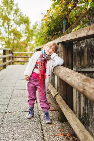 Outdoor portrait of a cute little girl wearing red trousers, colorful boots and white knitted jacket — Stock Photo, Image