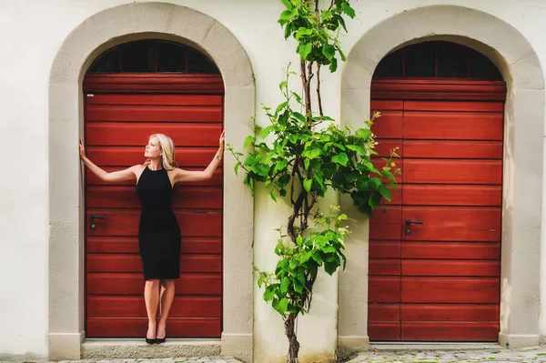 Retrato al aire libre de una joven rubia con vestido negro y zapatos de tacón alto — Foto de Stock