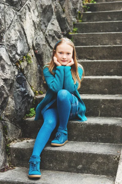 Outdoor fashion portrait of adorable little girl of 8-9 years old, wearing blue clothes and shoes, sitting on stairs in a city — Stock Photo, Image
