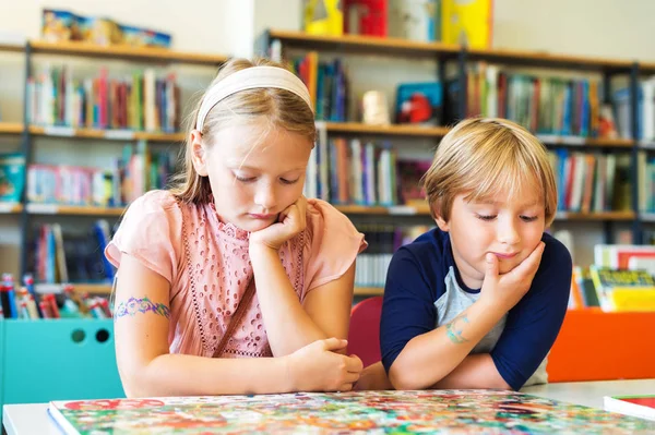 Duas crianças adoráveis, menina e seu irmão lendo livro em uma biblioteca — Fotografia de Stock