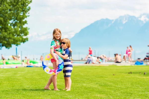 Twee schattige kinderen knuffelen elkaar staande bij het zwembad op een warme zomerdag, het dragen van zwemkleding — Stockfoto