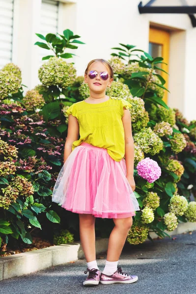 Retrato ao ar livre de menina bonito vestindo camisa verde, saia de tutu rosa, segurando óculos de sol — Fotografia de Stock