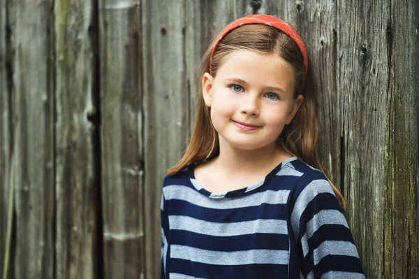 Ritratto all'aperto di carina bambina di 8-9 anni con i capelli castani, indossando top a strisce, in piedi contro il vecchio sfondo di legno — Foto Stock