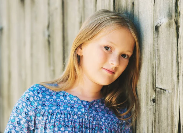 Ritratto ravvicinato di una graziosa bambina di 8-9 anni vestita di blu, appoggiata al vecchio muro di legno — Foto Stock