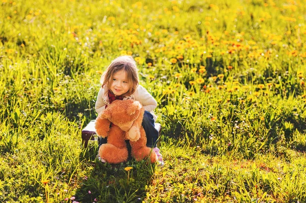 Adorable little girl of 3 years old playing with teddy bear outdoors on a very sunny day — Stock Photo, Image