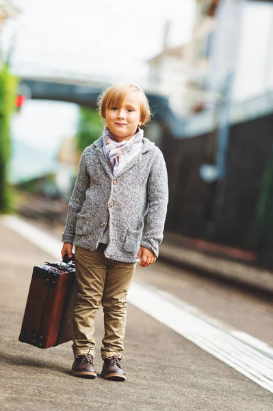 Entzückender kleiner Junge auf einem Bahnhof, der mit einem Koffer auf den Zug wartet — Stockfoto