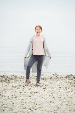  Gri pantolon ve uzun hırka giymiş 8-9 yaşında göl kenarında oynayan sevimli küçük kız